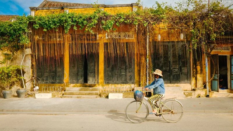 Một người đạp xe ngang qua ngôi nhà vàng cổ phủ dây leo với cửa gỗ ở phố cổ Hội An.
