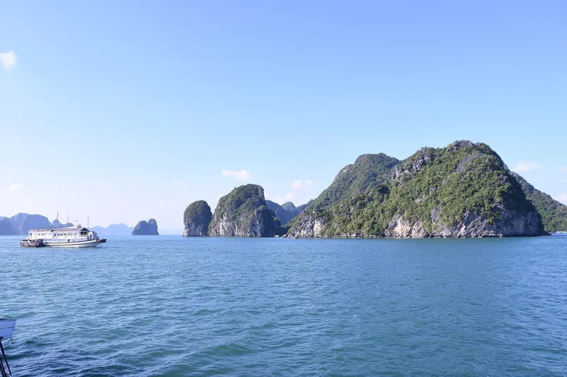 Những đảo đá vôi nhô lên từ mặt nước xanh với một tàu du lịch gần đó ở vịnh Hạ Long gần Hà Nội.