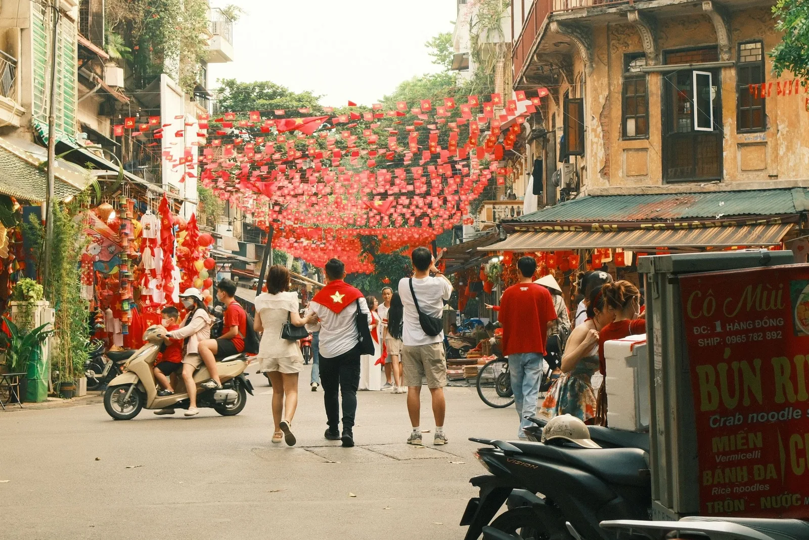 Đèn lồng và cờ đỏ giăng kín phố phường ở Phố Cổ Hà Nội, nơi người dân dạo bộ và chạy xe máy.