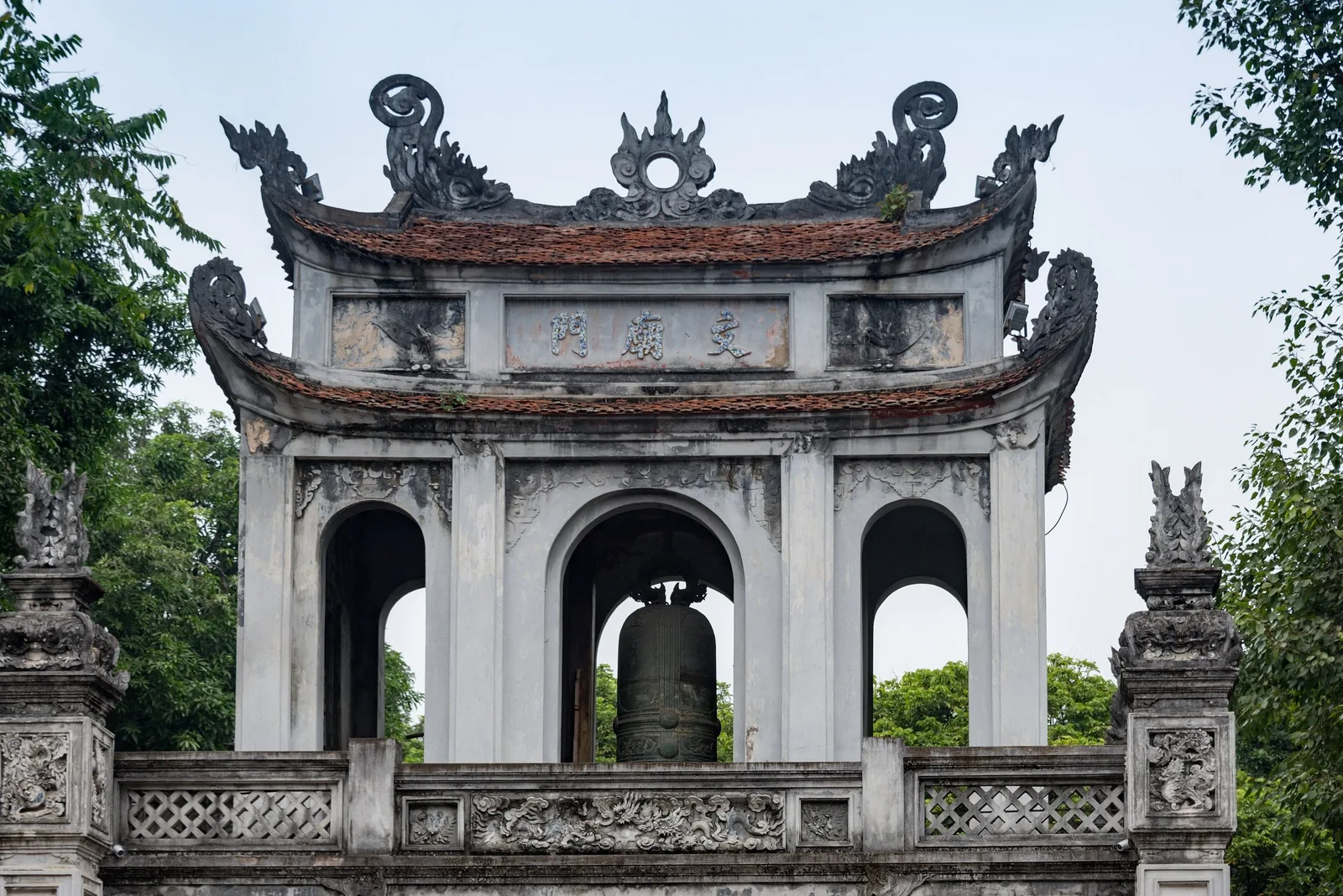 Cổng gác chuông chạm khắc tinh xảo của Văn Miếu Hà Nội, với chiếc chuông đồng bên dưới mái ngói cong.