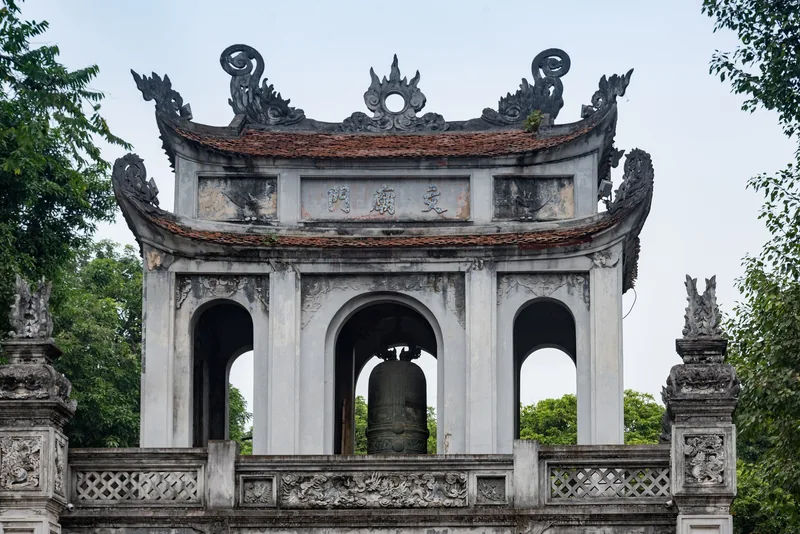Cổng gác chuông chạm khắc tinh xảo của Văn Miếu Hà Nội, với chiếc chuông đồng bên dưới mái ngói cong.